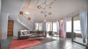 A spacious living area with a modern staircase, a large sofa, and a dining table. - Exceptional Corsican villa in the Gulf of Porto-Vecchio with its feet in the water (Porto-Vecchio)