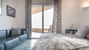 A modern bedroom with a large bed, a sofa, and a balcony with patterned curtains. - Exceptional Corsican villa in the Gulf of Porto-Vecchio with its feet in the water (Porto-Vecchio)