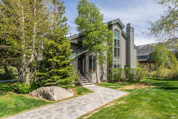 A two-story house with a stone pathway leading to the front door, surrounded by lush greenery and trees.