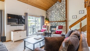 Ein gemütliches Wohnzimmer mit Steinwand, Kamin, Flachbildfernseher und bequemen Sitzmöglichkeiten.