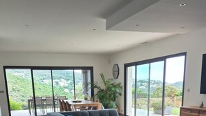A spacious living room with a large sectional sofa, wooden flooring, and large sliding glass doors leading to a balcony with a scenic view.