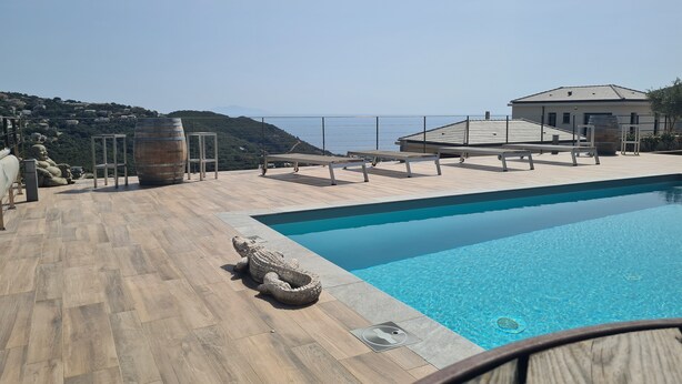 A rooftop pool with a clear view of the sea, wooden deck, and lounge chairs.