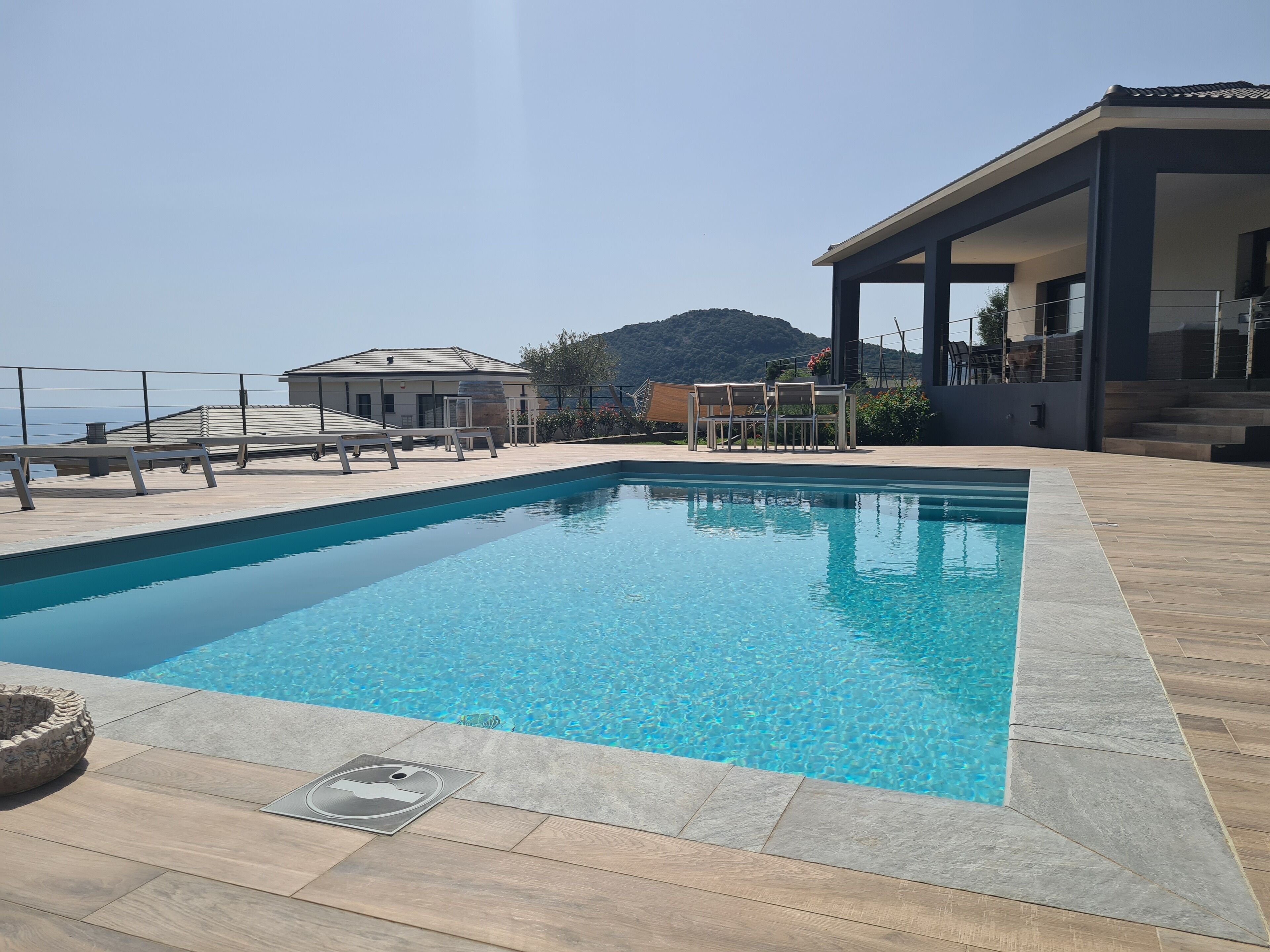 A swimming pool with a wooden deck, a covered seating area, and a view of a mountain.