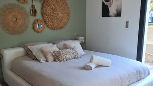 A modern bedroom with a large bed, decorative wall hangings, and a framed photograph.