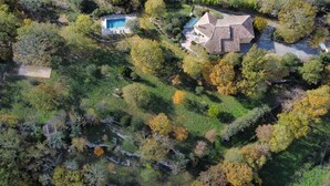 Luchtbeeld van een bezit met zwembad, een groot huis met pannendak en omliggende bebossing.
