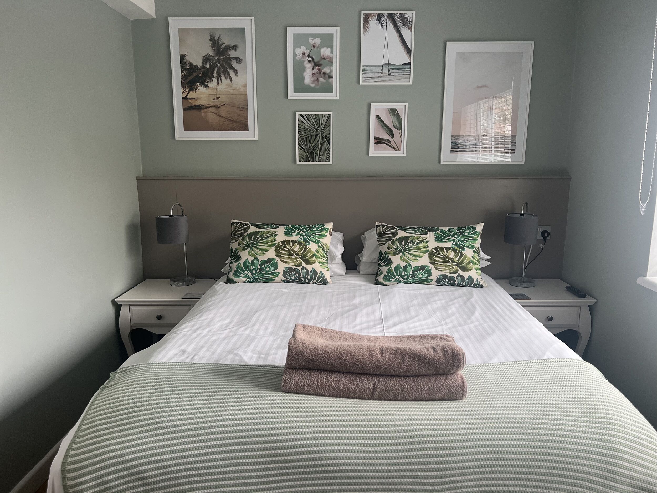 A neatly made bed with a striped bedspread, two pillows with a tropical leaf pattern, and a pair of folded towels.