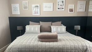 A neatly made bed with a quilted bedspread, two pillows with feather embroidery, and a folded blanket on top. - Forever Summer (Lymington)