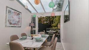 A dining area with a glass ceiling, a table set with plates, glasses, and a bottle, and chairs with a unique design. - Forever Summer (Lymington)