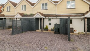 A row of three two-story houses with a gravel driveway and a black gate. - Forever Summer (Lymington)