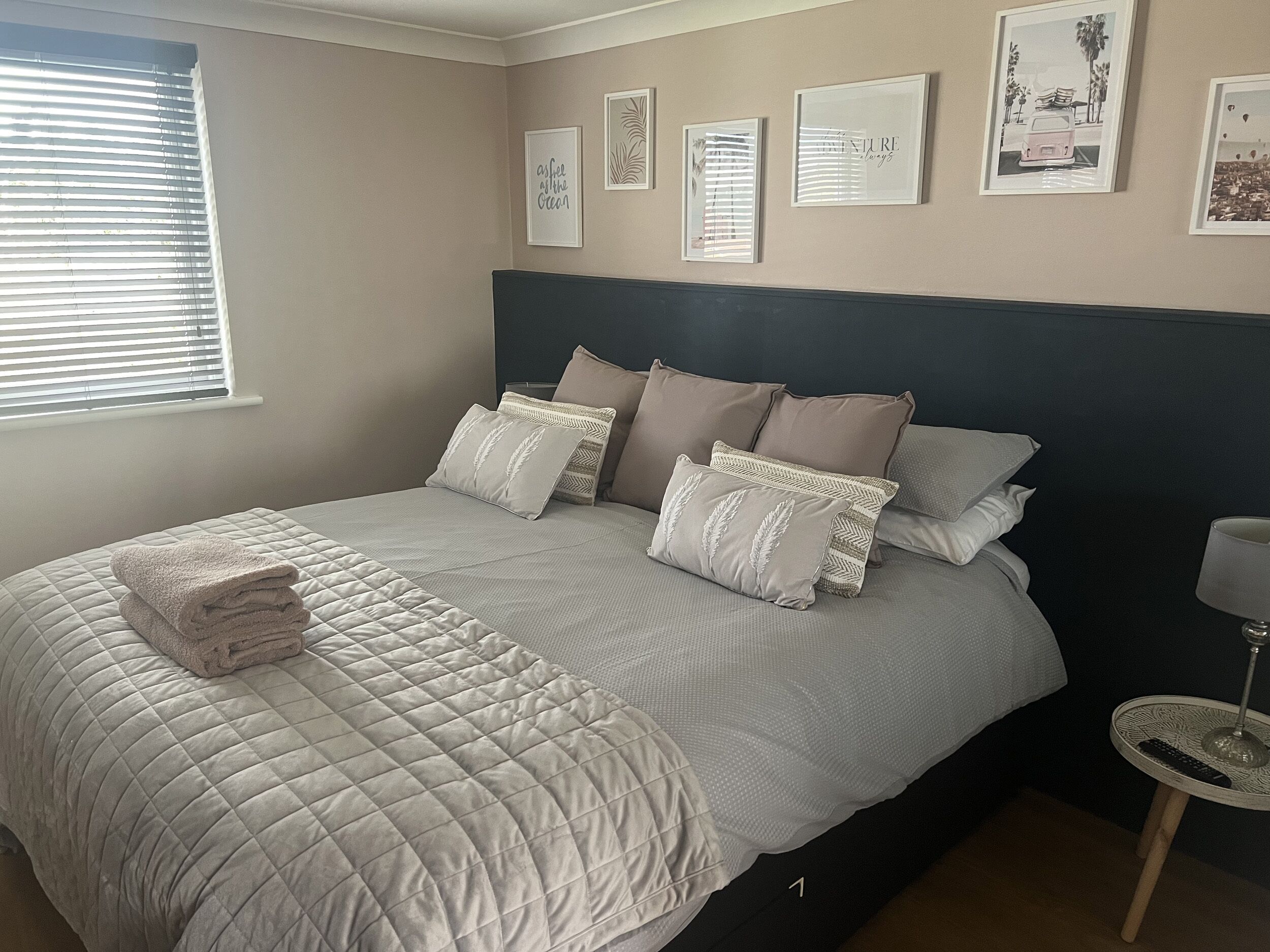 A bedroom with a bed, pillows, a bedside table with a lamp, and framed pictures on the wall.