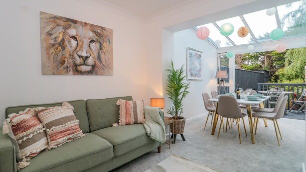 A living room with a green sofa, a large abstract painting, and a dining area with a table set for four. - Forever Summer (Lymington)