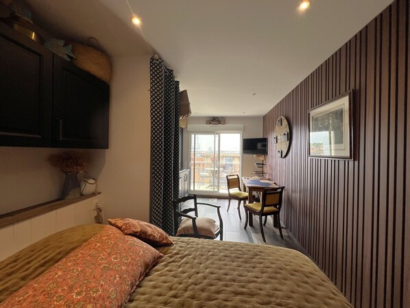 A bedroom with a bed, a desk with a chair, a TV, and a window.