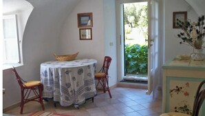A dining area with a round table, two chairs, and a basket. There are framed pictures on the wall, a window with a view of greenery, and a door leading outside. - The Sea - White House (Camporosso)