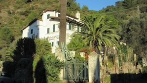 A two-story house with a white facade, green shutters, and a stone wall. - The Sea - White House (Camporosso)