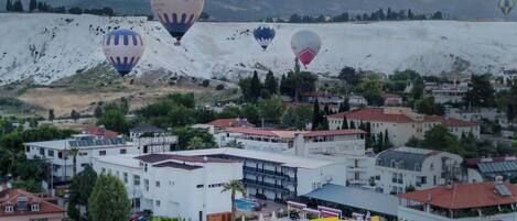 Un resort con varias edificaciones, una piscina y globos aerostáticos al fondo.