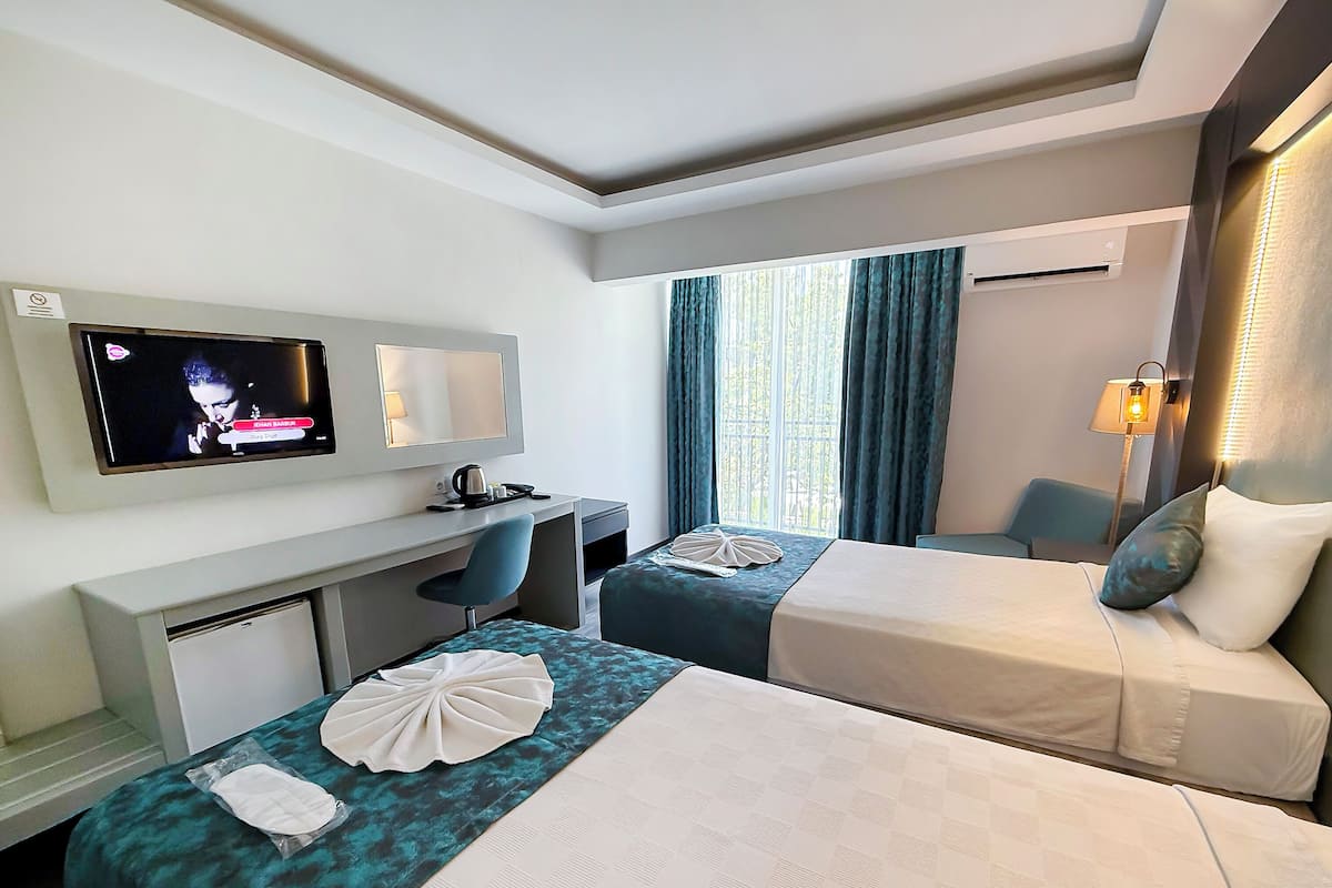A hotel room with two beds, a desk with a chair, a television, and a window with curtains.