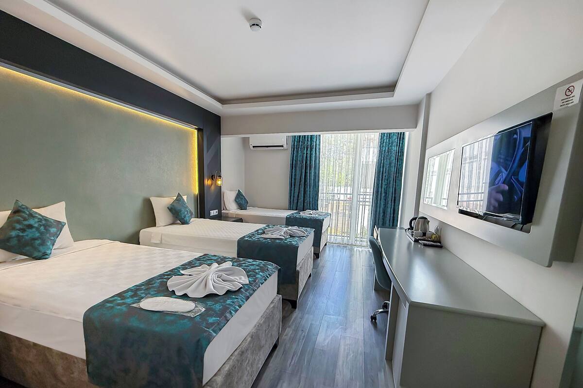 A hotel room with two beds, a desk, a TV, and a balcony with curtains.