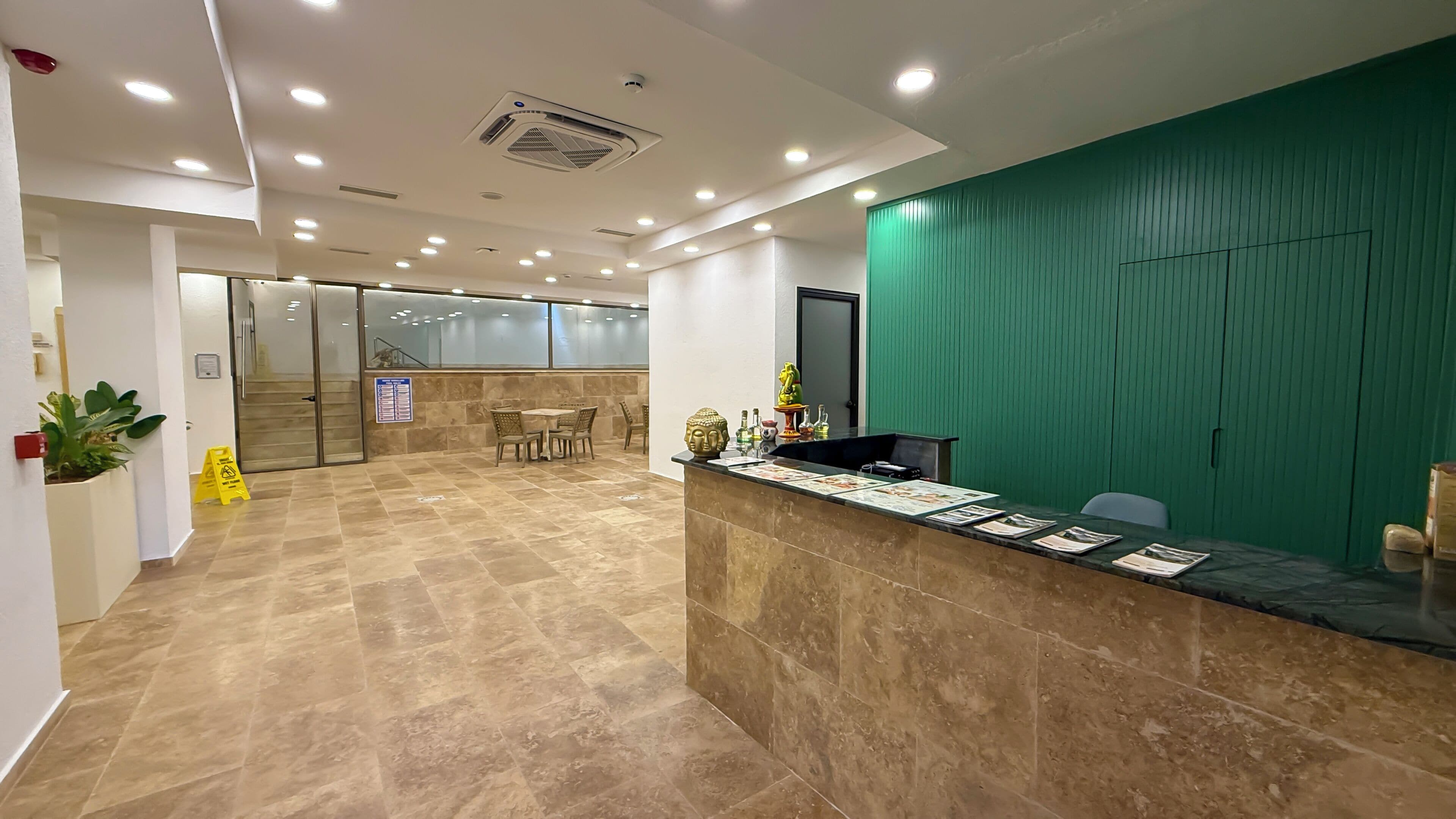 A reception area with a marble floor, a reception desk, a green wall, and a staircase in the background.