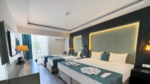 Habitación de hotel con dos camas, un escritorio, una lámpara y vistas al exterior.