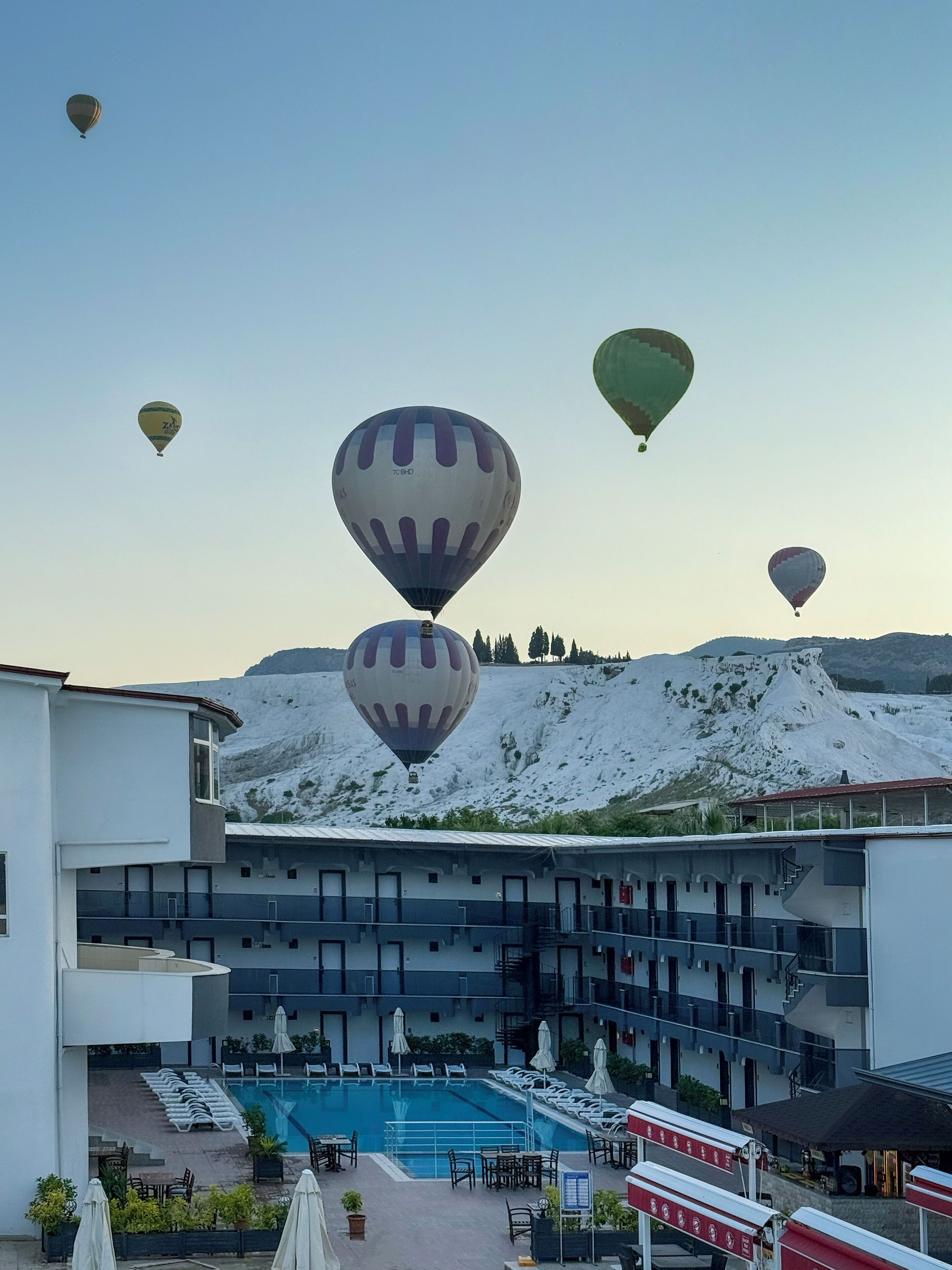 Een hotel met een zwembad, terras en luchtballonnen op de achtergrond.