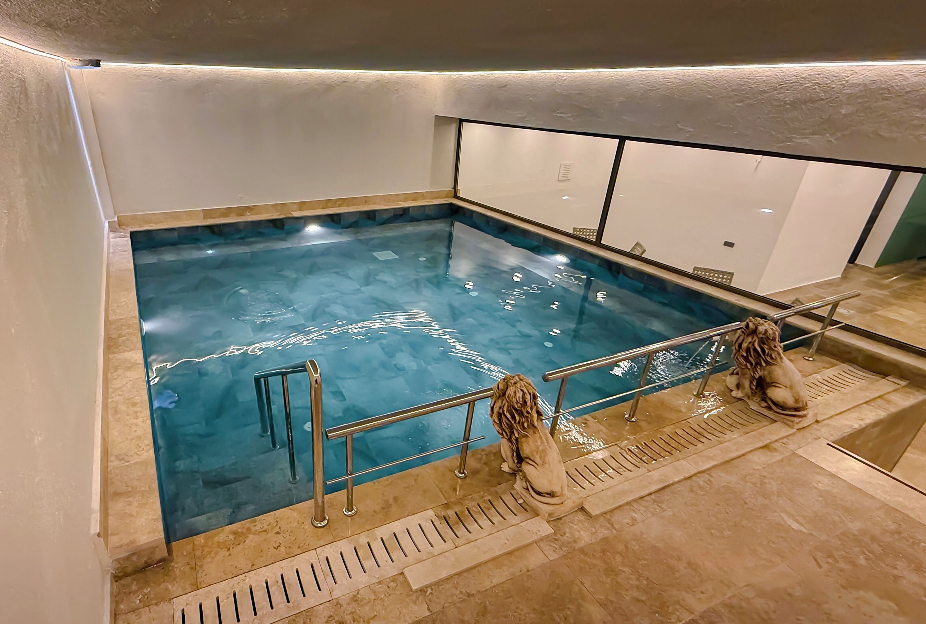 Une piscine à fond de verre, entourée d’une rambarde en métal et dotée d’un sol en pierre.