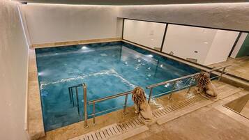 A swimming pool with a glass bottom, surrounded by a metal railing and a stone floor.