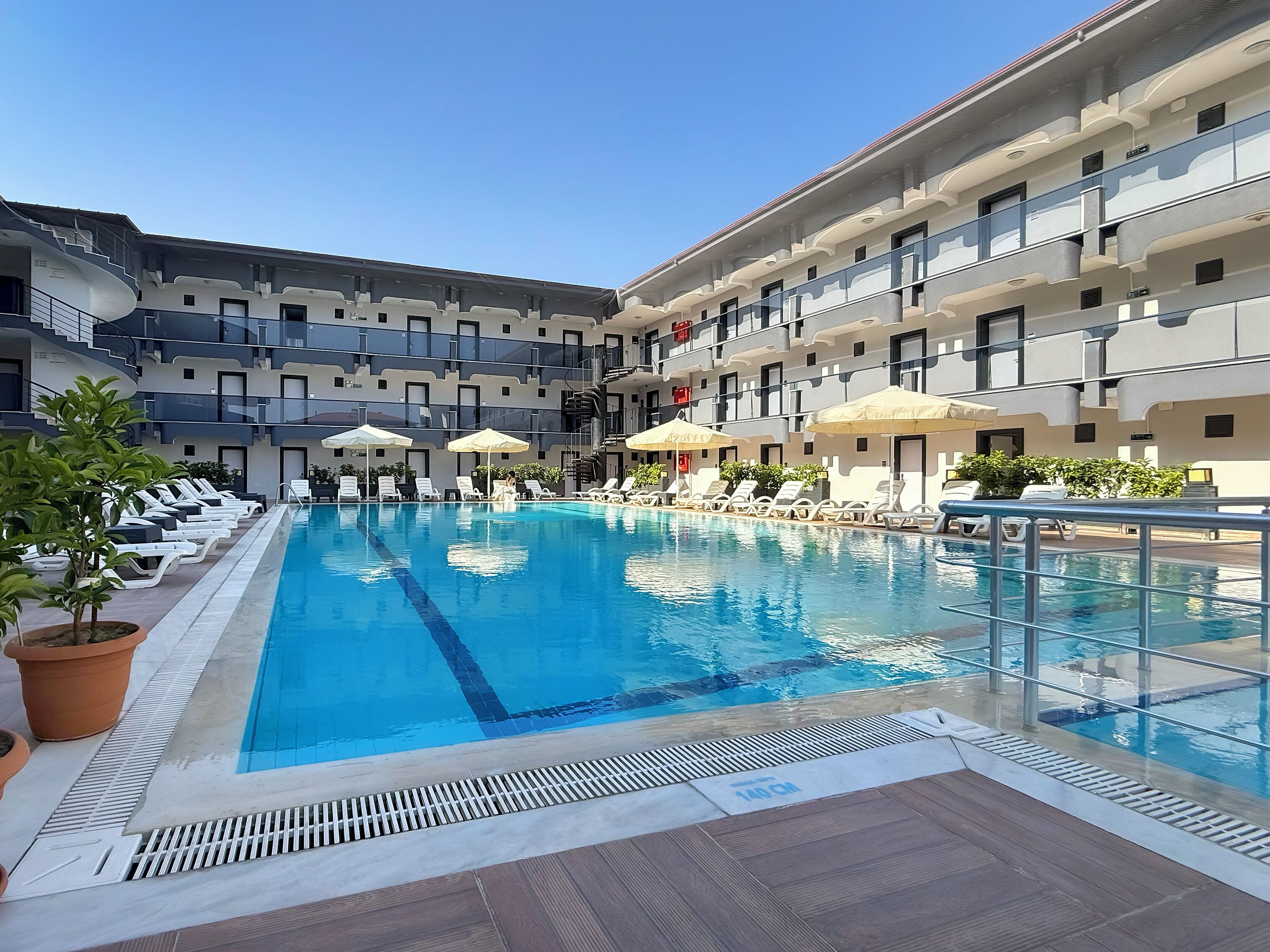 A swimming pool with lounge chairs and umbrellas, surrounded by a multi-story building with balconies.
