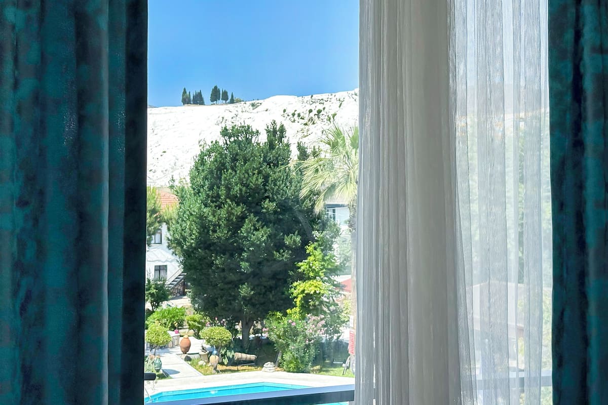 A view through curtains of a pool area with a mountain backdrop.