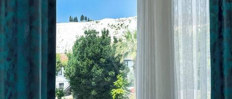 A view through curtains of a pool area with a mountain backdrop.