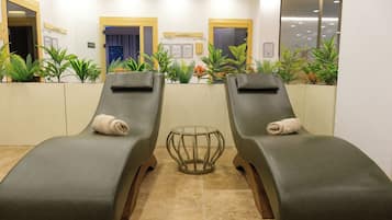 Two reclining chairs with towels, a glass table, and potted plants in a well-lit indoor area.