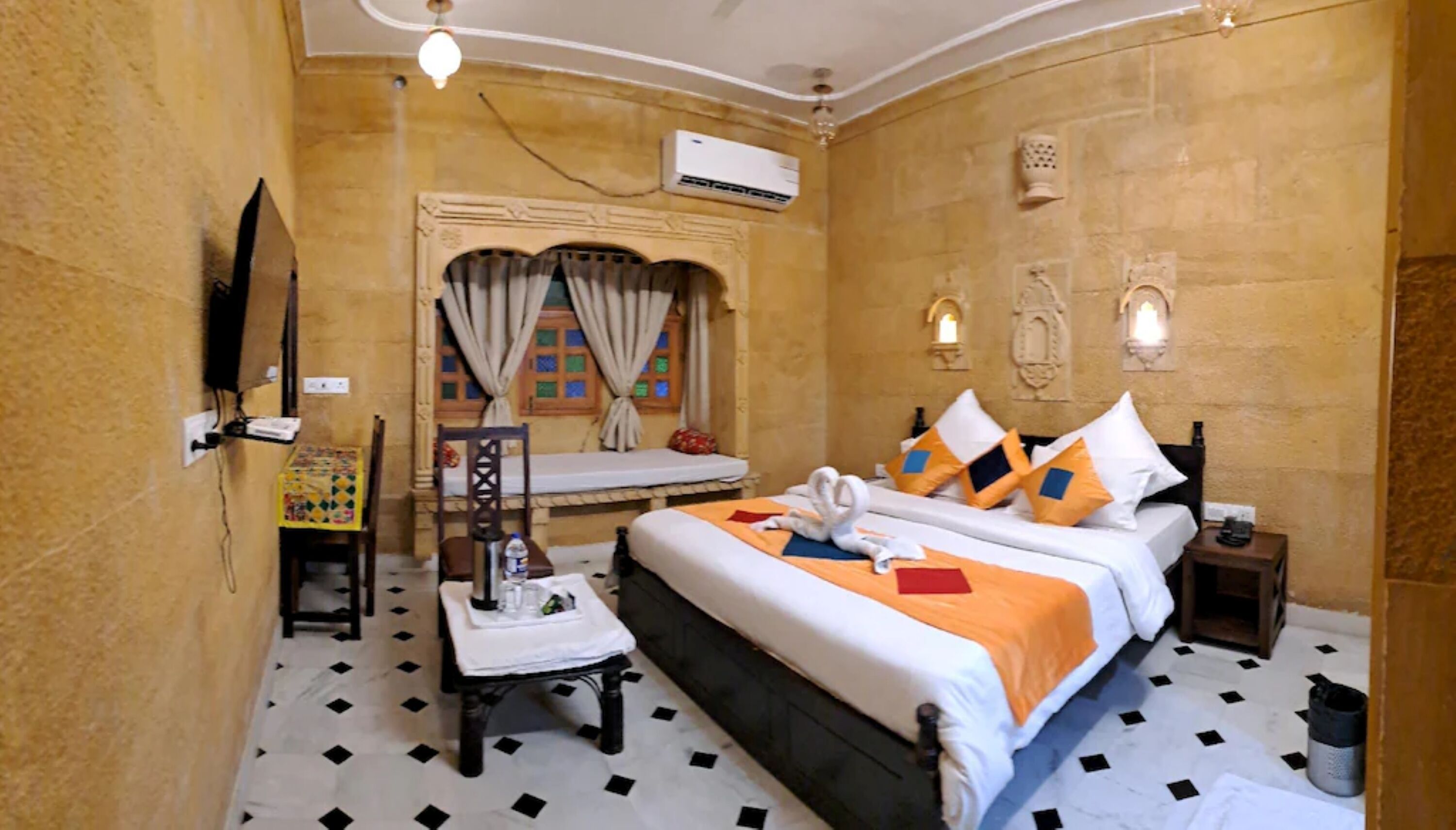 A hotel room with a bed, a small table, a chair, an air conditioning unit, and a window with curtains.