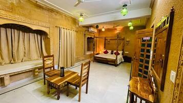 A room with a bed, a dining table with chairs, a bench, and a ceiling fan.