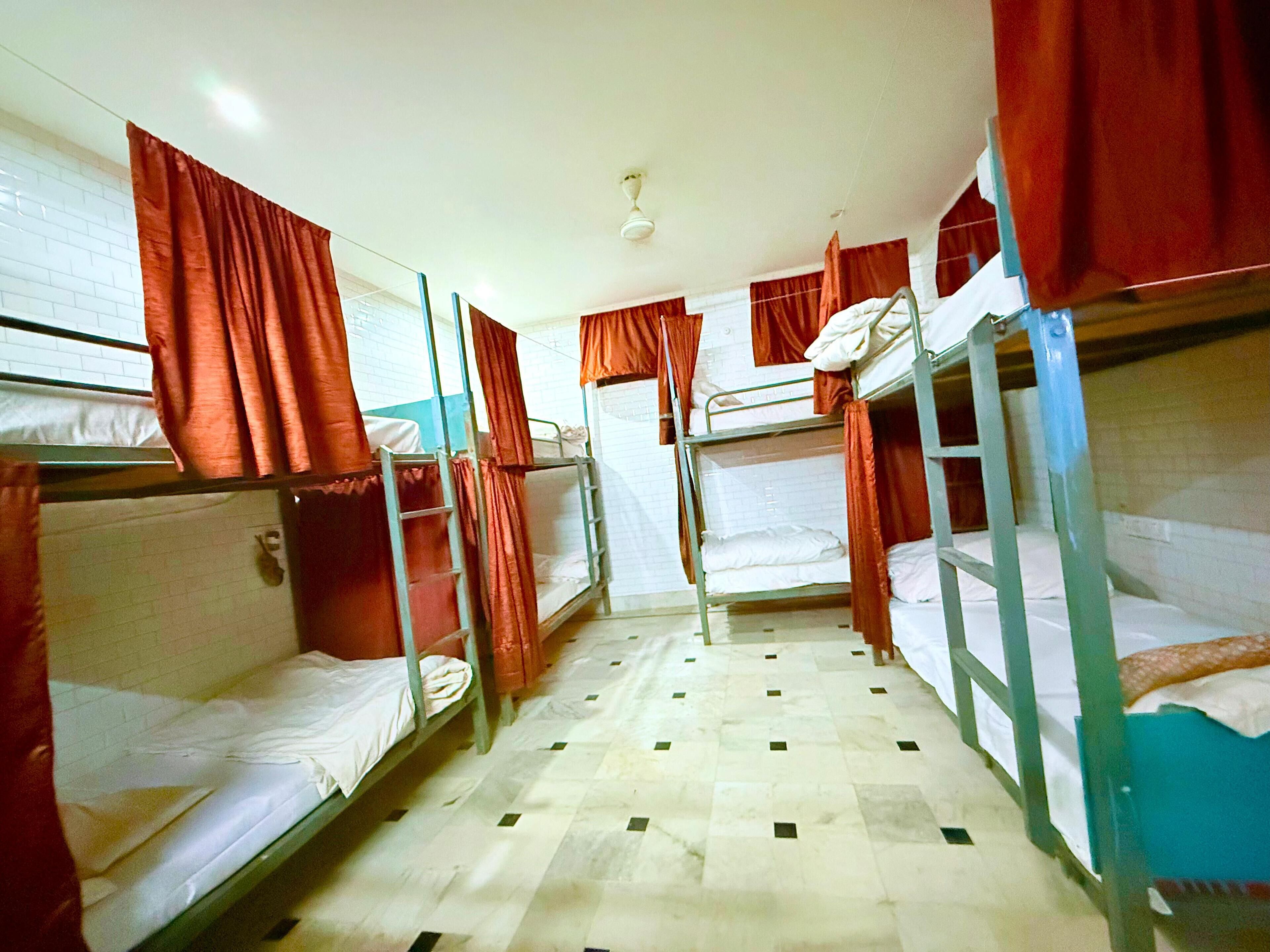 A dormitory room with bunk beds, red curtains, a tiled floor, and a ceiling fan.