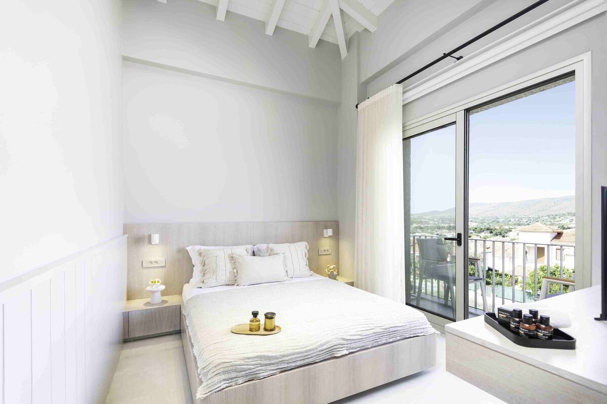 Une chambre moderne avec un grand lit, des tables de chevet, une fenêtre donnant sur la ville et un balcon.
