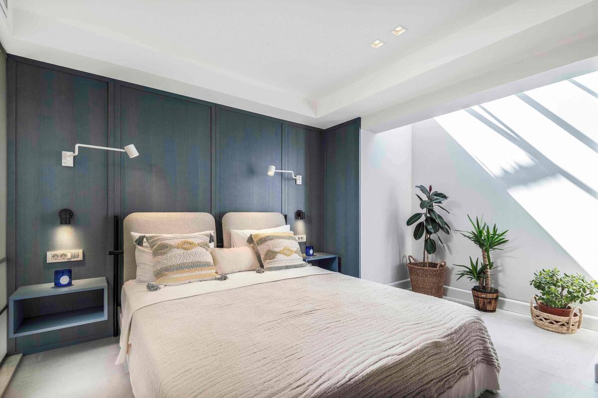 Une chambre moderne avec un grand lit, deux tables de chevet avec des lampes et des plantes en pot.