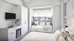 Un dormitorio con cama, televisor, ventana con vistas y mesita de noche.