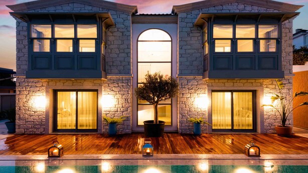 Una casa de dos pisos con paredes de piedra, ventanas grandes y una piscina en la parte frontal.