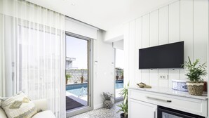 Cocina moderna con televisor de pantalla plana, zona de comedor con mesa blanca y sofá, y vista a una piscina a través de amplios ventanales.