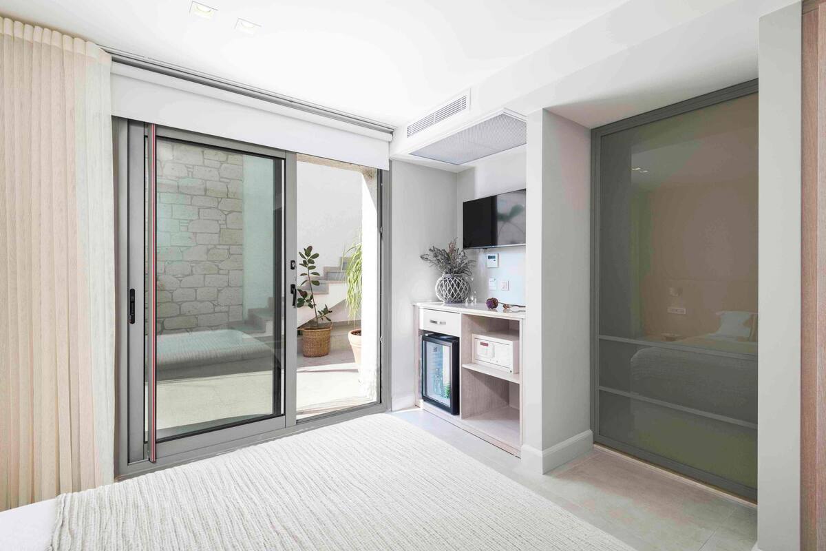 Une chambre moderne dotée d’une porte-fenêtre coulissante donnant sur un balcon, d’un petit coin cuisine et d’un téléviseur fixé au mur.