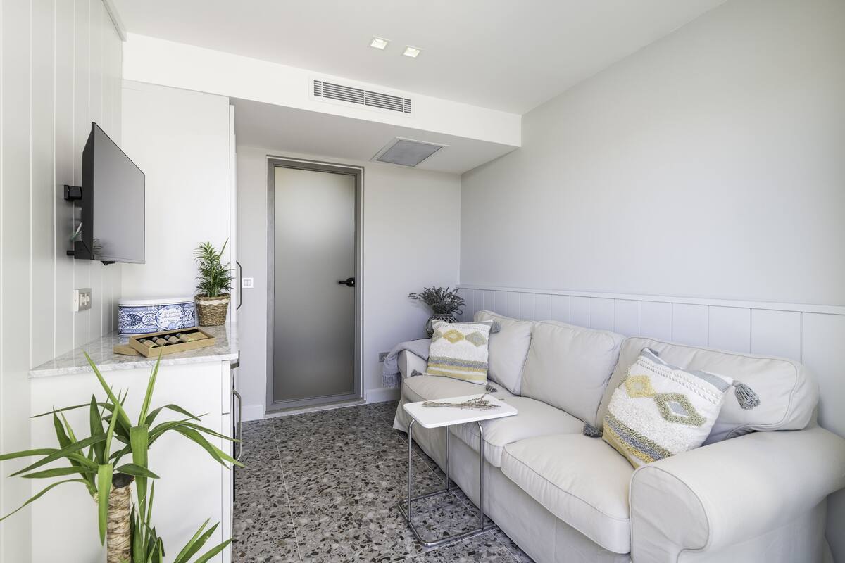 Un salon moderne avec un canapé blanc, un téléviseur à écran plat fixé au mur et une petite table d’appoint.