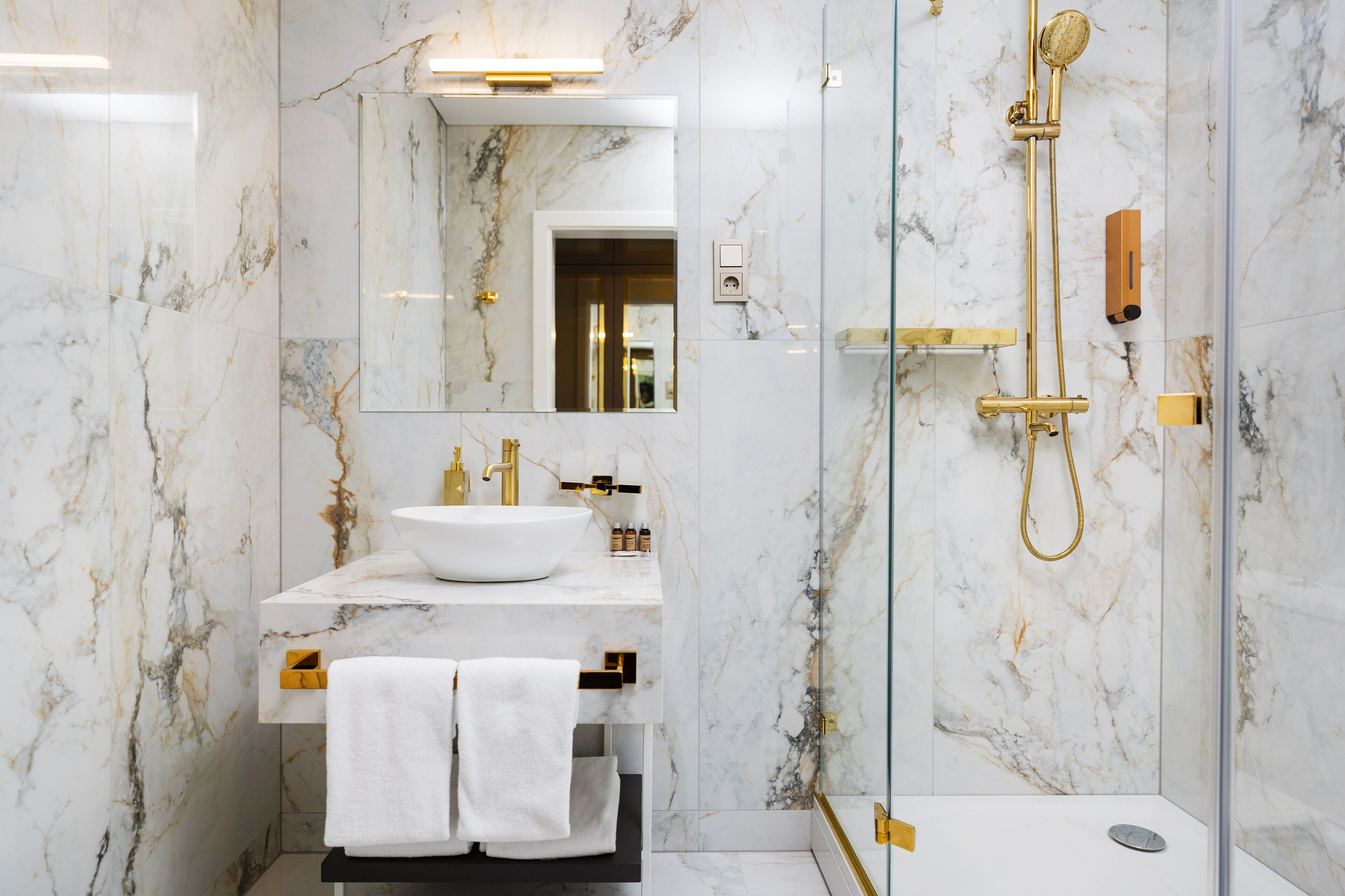 A modern bathroom with a marble sink, gold fixtures, and a glass-enclosed shower.