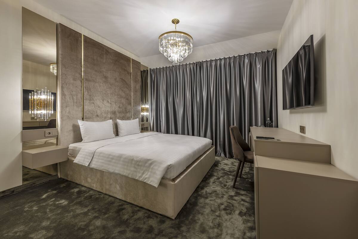 A modern bedroom with a large bed, bedside tables, a TV, and a chandelier.