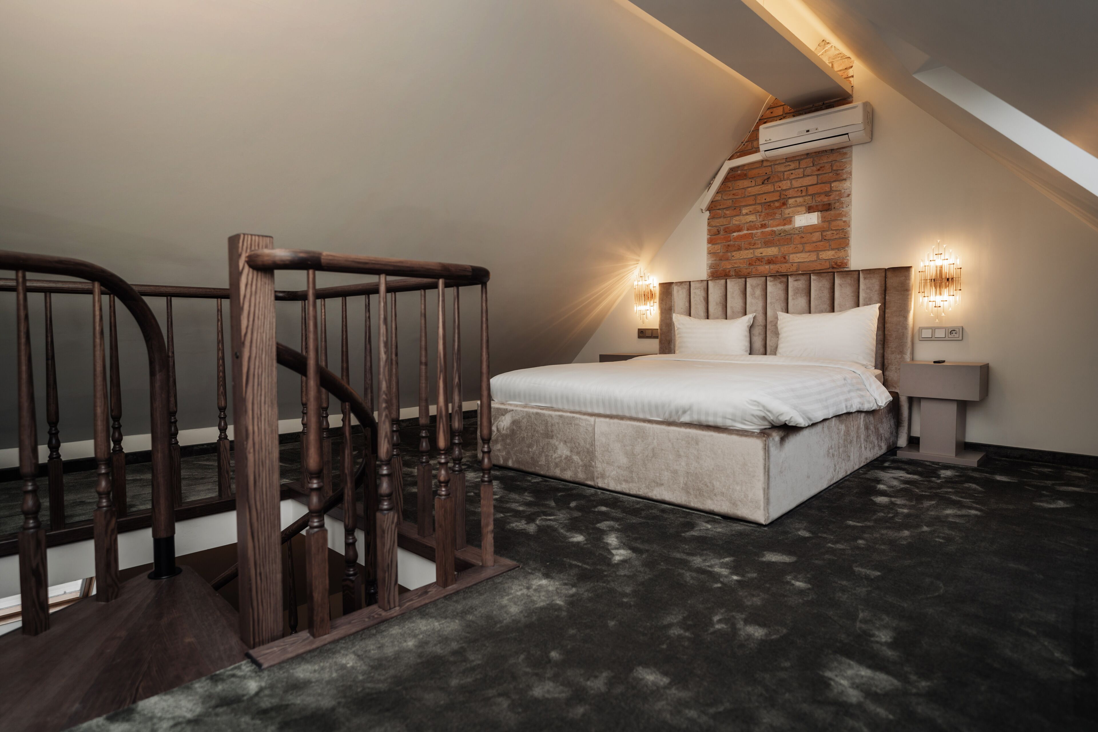 Un dormitorio con cama, una escalera de madera, una pared de ladrillo y un ventilador de techo.