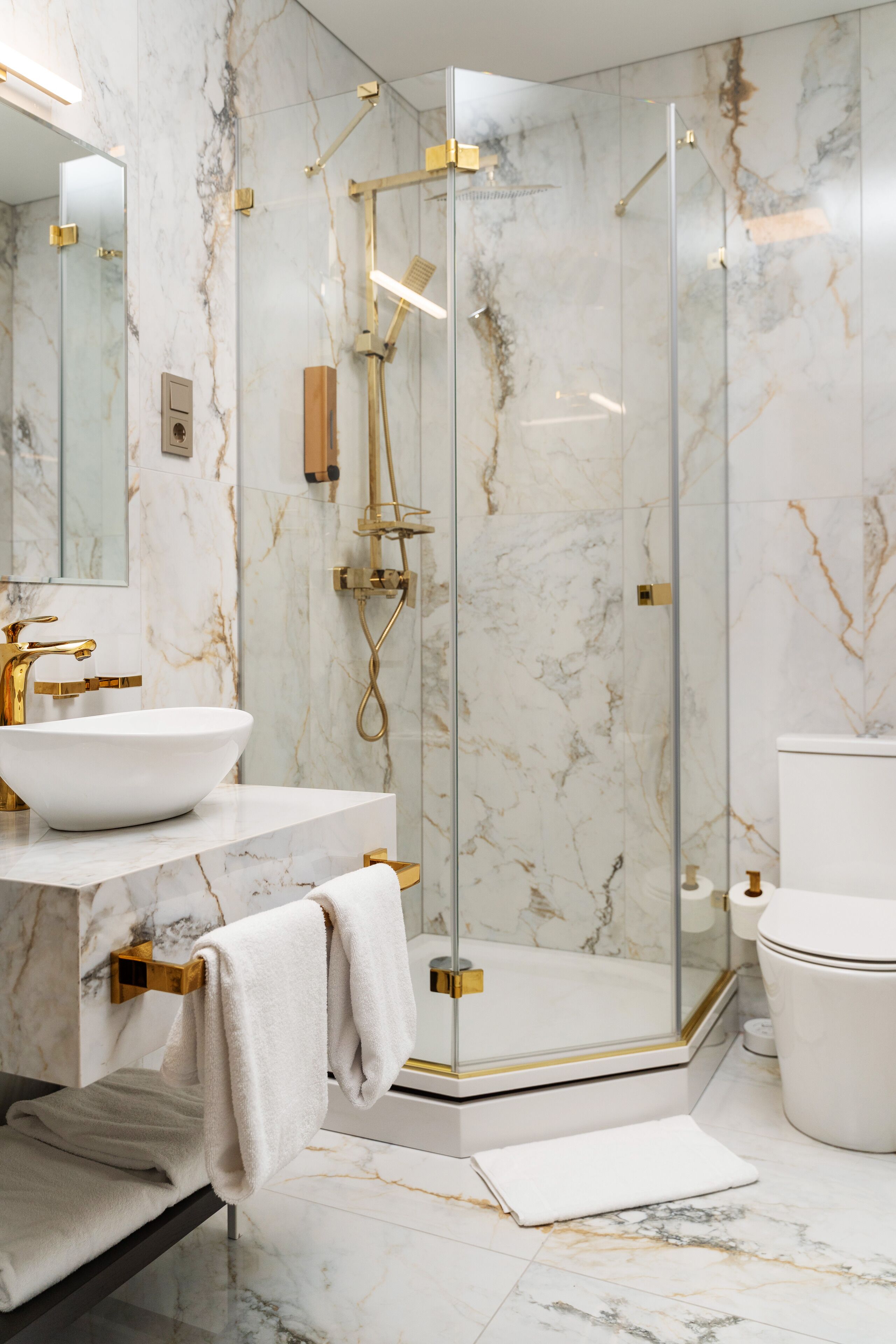 Un baño moderno con ducha envuelta en vidrio, lavamanos blanco y detalles dorados.