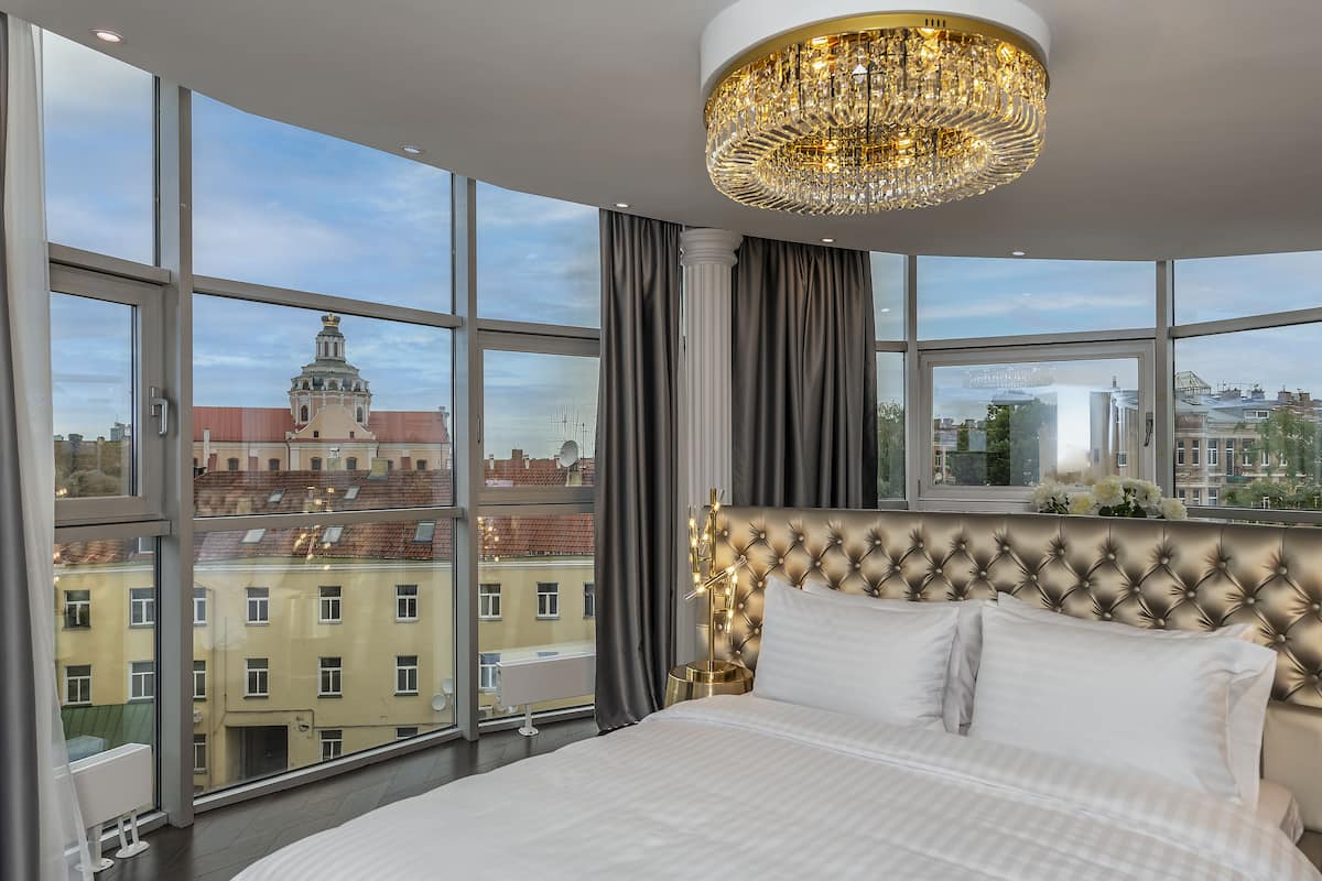 A bedroom with a large window, a tufted headboard, and a chandelier.