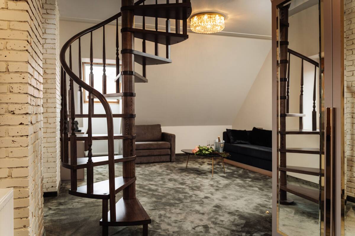 A spiral staircase in a loft-style room with a brick wall, a dark-colored sofa, and a small table with flowers.