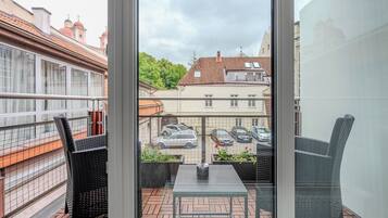 Een balkon met rieten stoelen, een tafel en uitzicht op geparkeerde auto's en gebouwen.