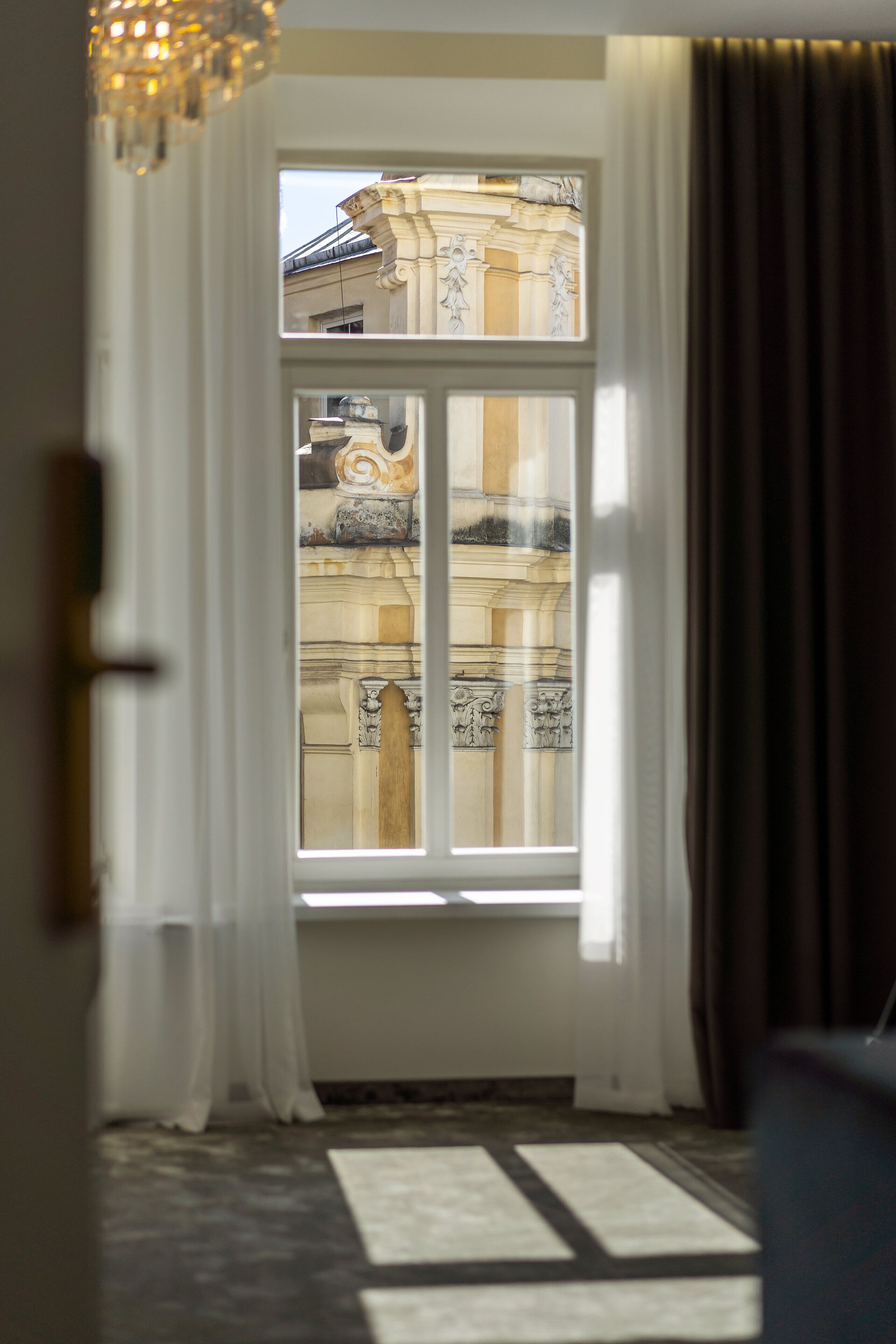A room with a large window, white curtains, and a patterned carpet.