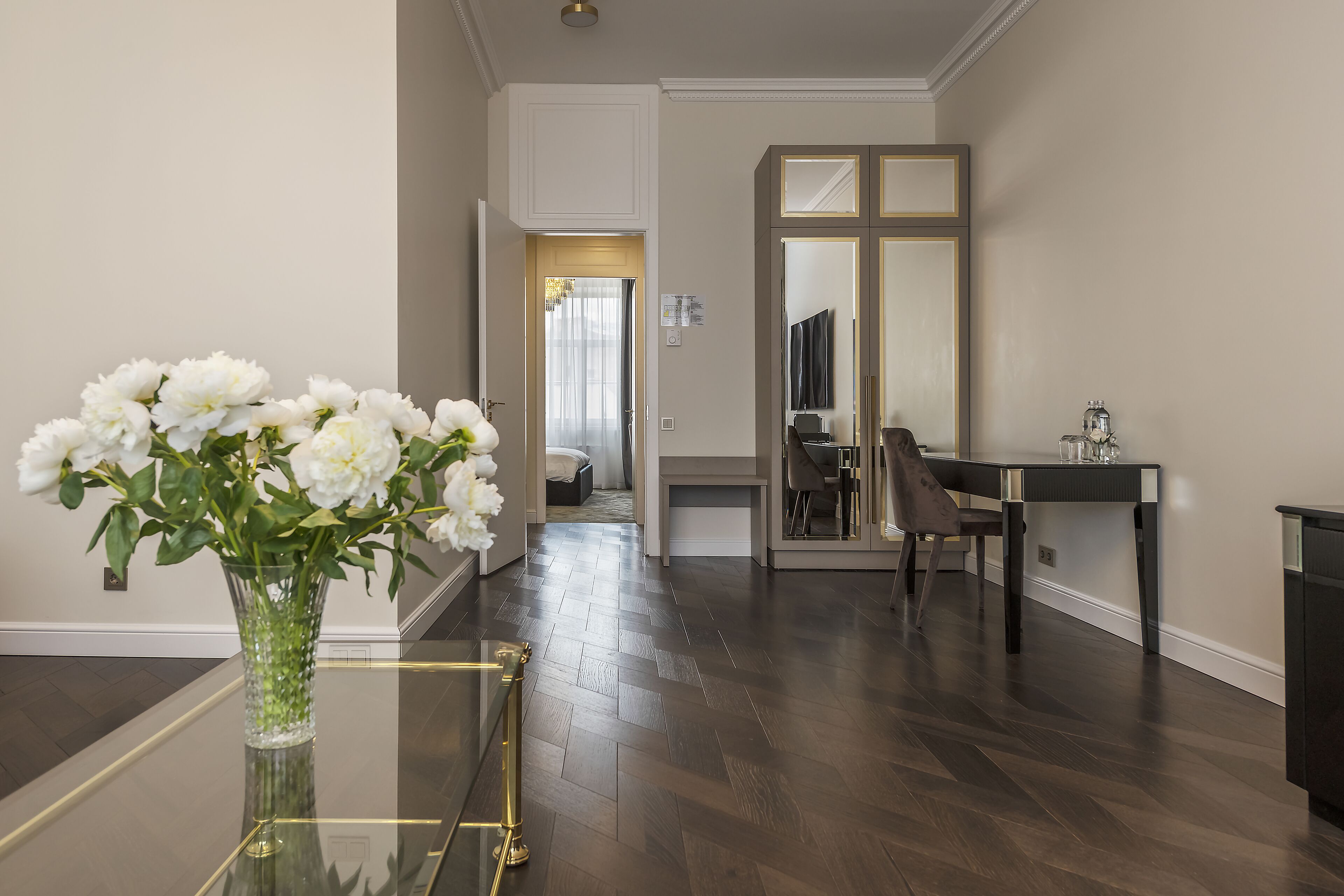 Un interior moderno con una mesa de cristal, un florero de flores blancas, un suelo de madera oscura y un espejo con marco negro.