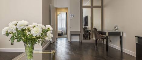Un interior moderno con una mesa de cristal, un florero de flores blancas, un suelo de madera oscura y un espejo con marco negro.
